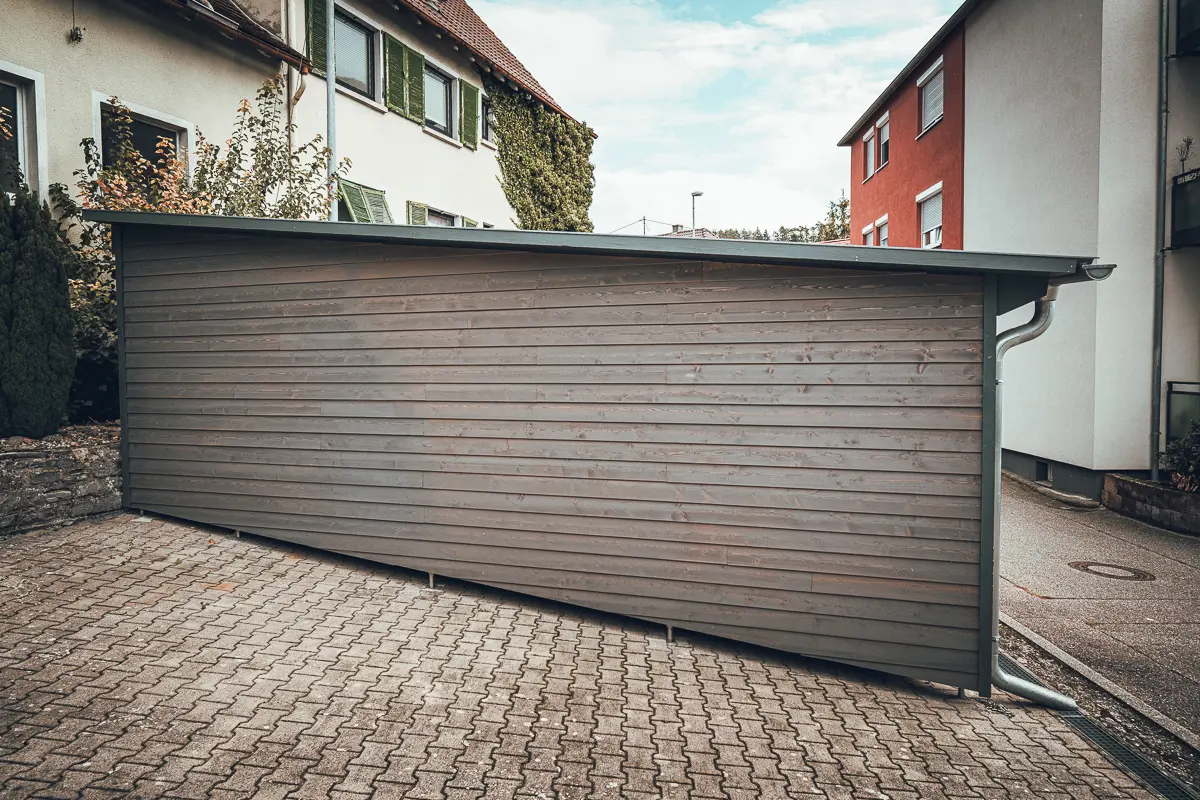 Lauffers klassisches Bauprojekt: moderner Carport in Holzverschalung mit Stützfüßen für den konstruktiven Holzschutz.